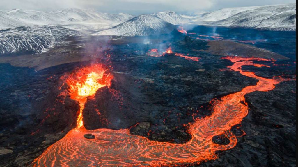 Iceland’s Volcanic Spine: Following the Rift That Built the Earth Molten lava flowing across a dark volcanic field with snow‑covered mountains in the background