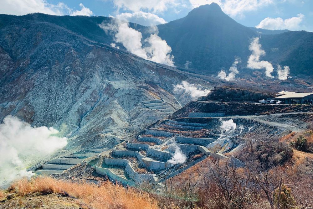 Aerial view of Hakone’s geothermal slopes with steaming vents and terraced volcanic terrain.