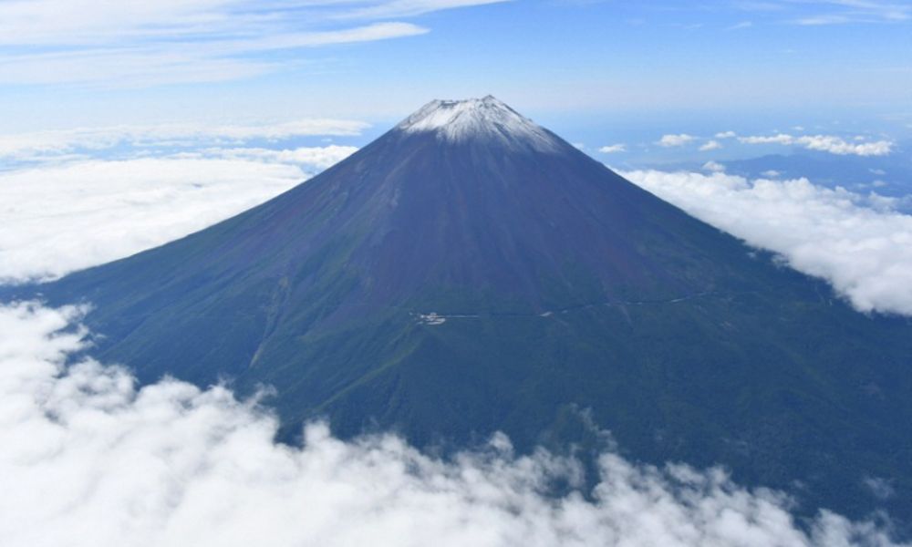 Distant view of Mount Fuji showing its grey volcanic slopes, dark rock textures, and a light snow cap at the summit.