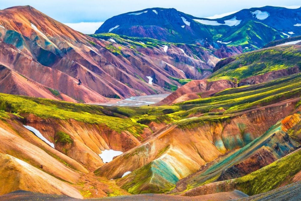 Colorful rhyolite mountains of Landmannalaugar, Iceland, with red, orange, green, and purple slopes under a blue sky.