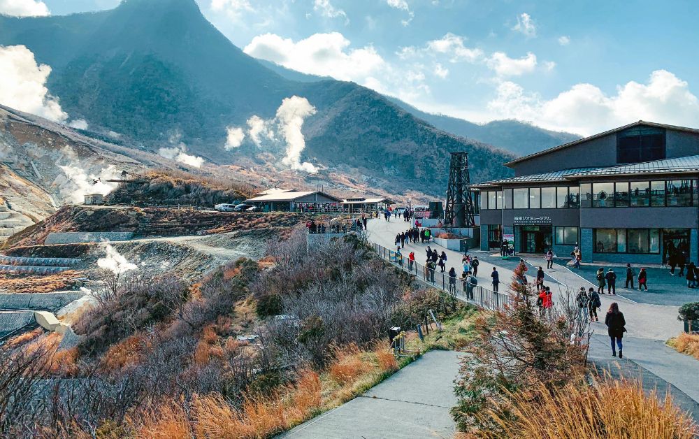 Distant view of Owakudani integrated into a green mountainside, with soft steam rising from geothermal vents.