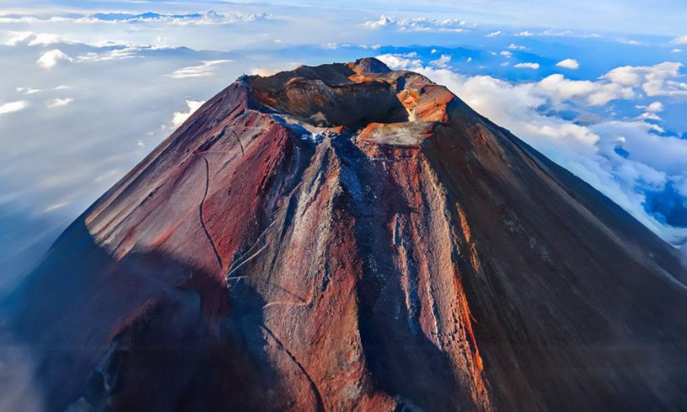 Aerial view of Mount Fuji’s summit showing the central crater, steep volcanic walls, and radiating lava formations.