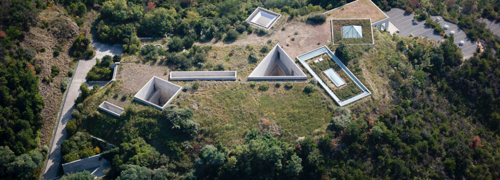 Aerial view of Chichu Art Museum on Naoshima, showing geometric concrete skylights set into a green hillside above the museum.
