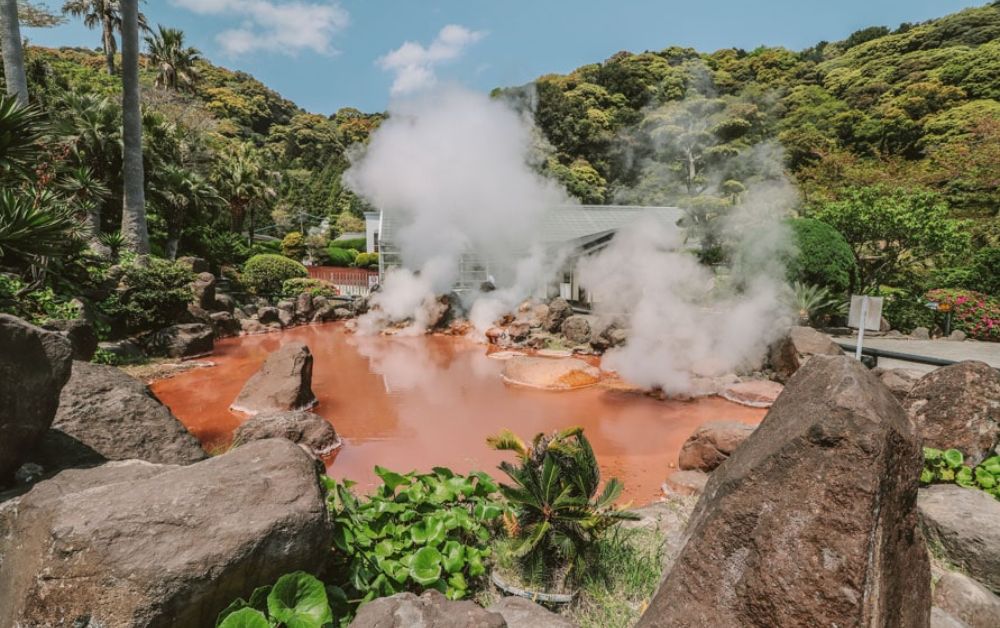 One of Beppu’s jigoku, Chinoike Jigoku in iron‑rich red, with steam rising in the cool morning air.