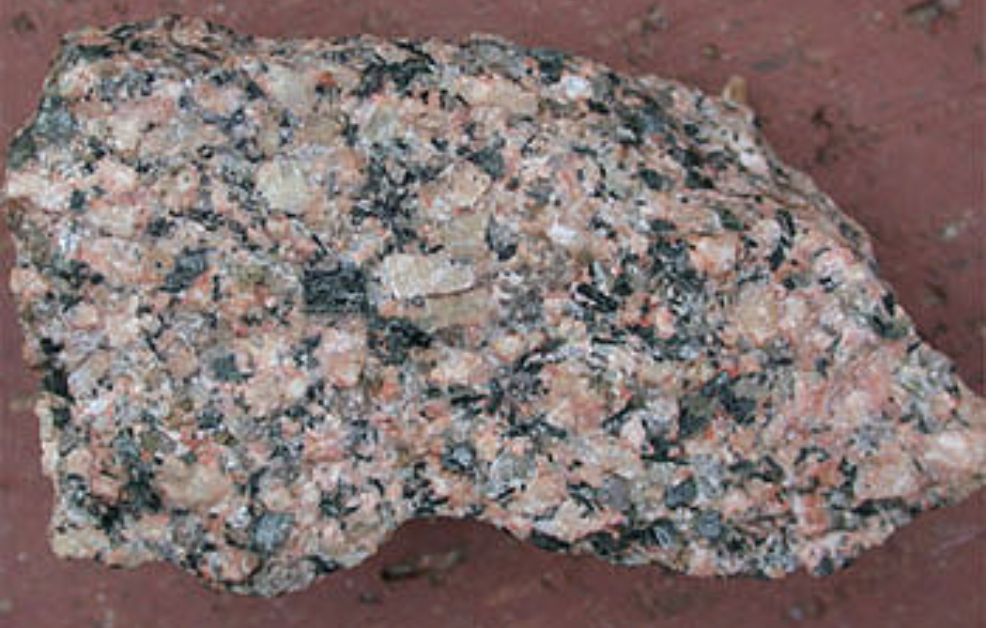 Close-up of a pinkish-grey granite specimen showing pink feldspar, translucent quartz, and dark biotite mica crystals.