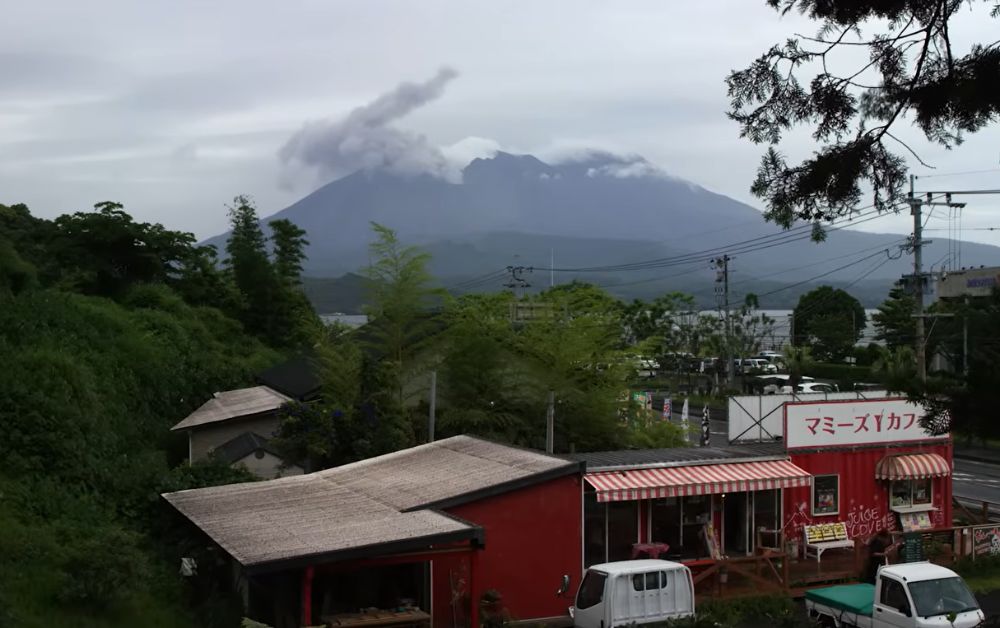 Sakurajima releasing an ash column, with the city of Kagoshima visible in the foreground across the bay.