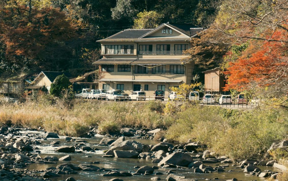 Steep alpine river flowing from a granite ridge at dawn, with a small ryokan and onsen building at the base of the valley in Japan’s Alps.