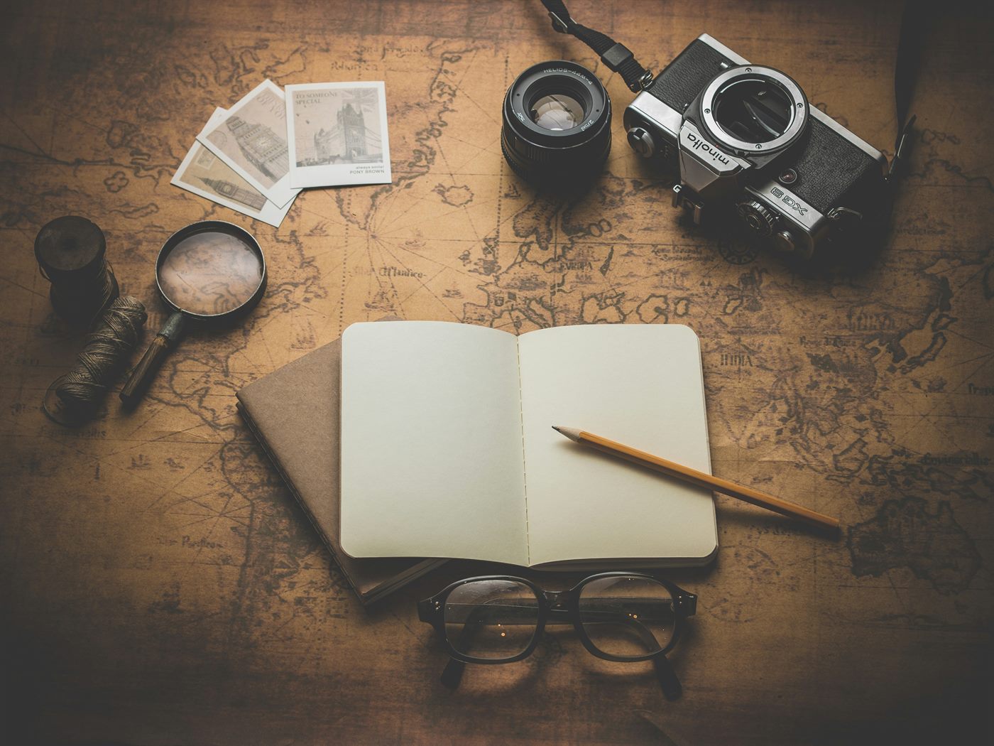 Flat lay of travel and field study materials: notebook, pencil, camera and lens on a wooden surface