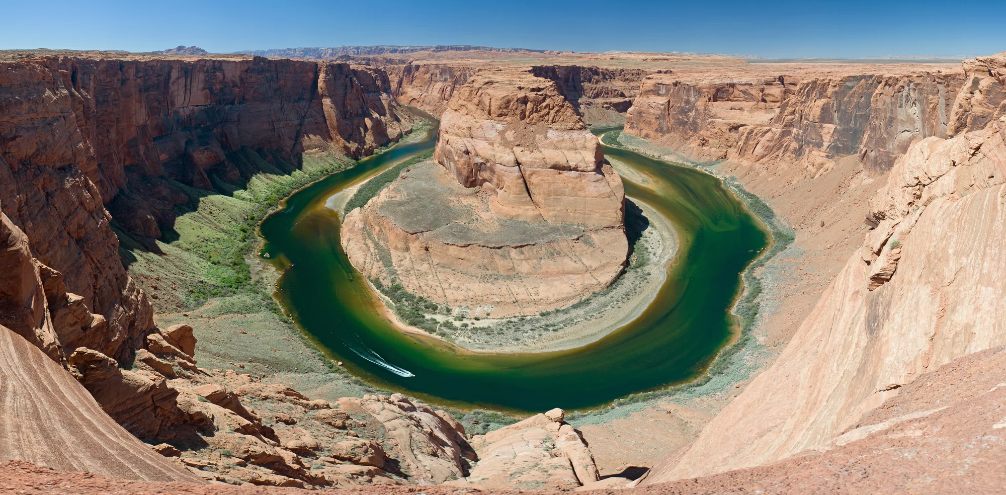 View of the Colorado River at the base of Horseshoe Bend, with a small raft for scale showing the depth of the canyon.